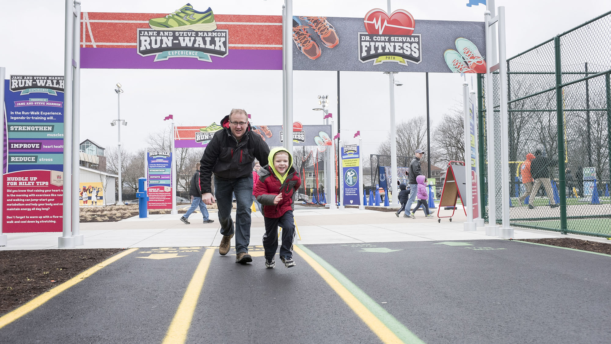 Grown-up and child running on paved track.