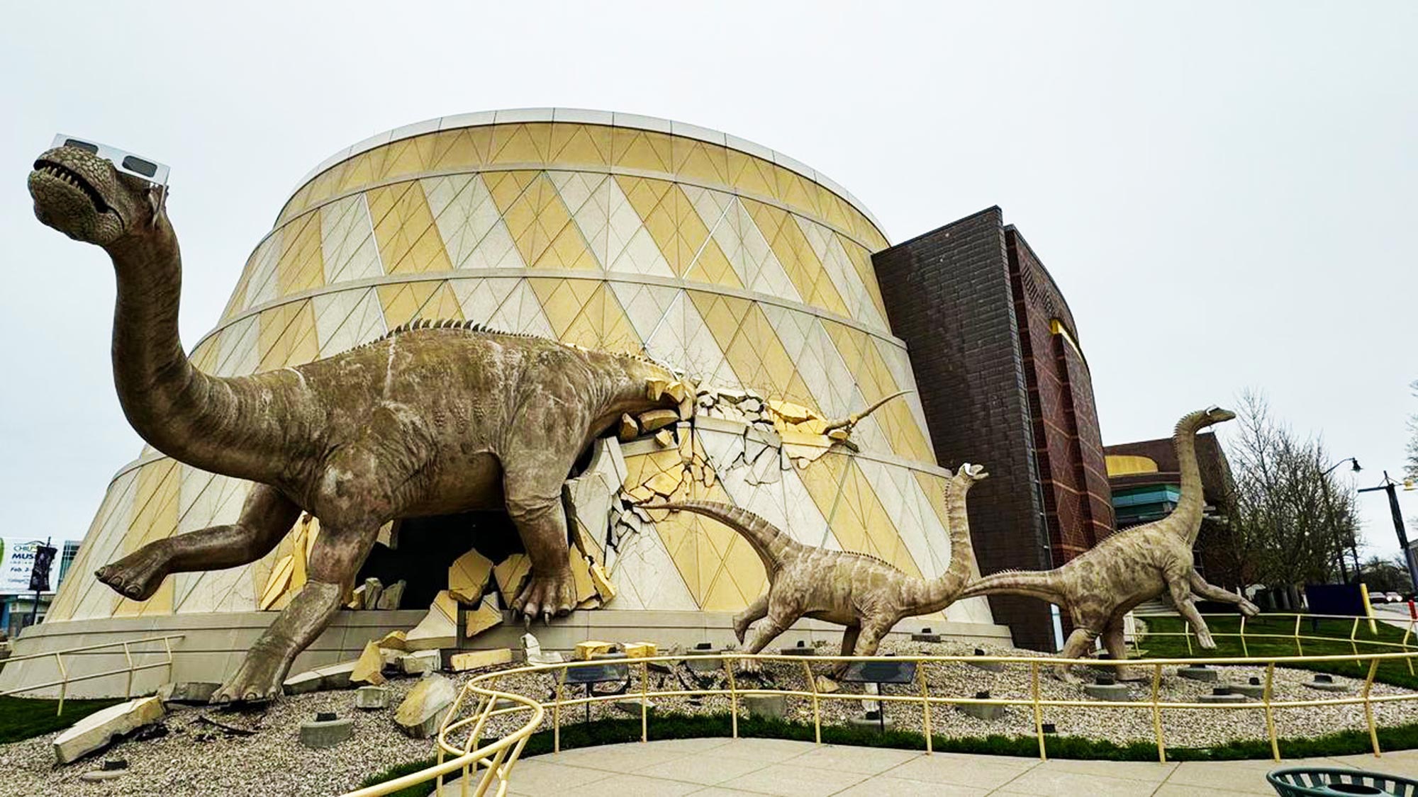Dinosaur statues wearing giant eclipse viewing glasses.