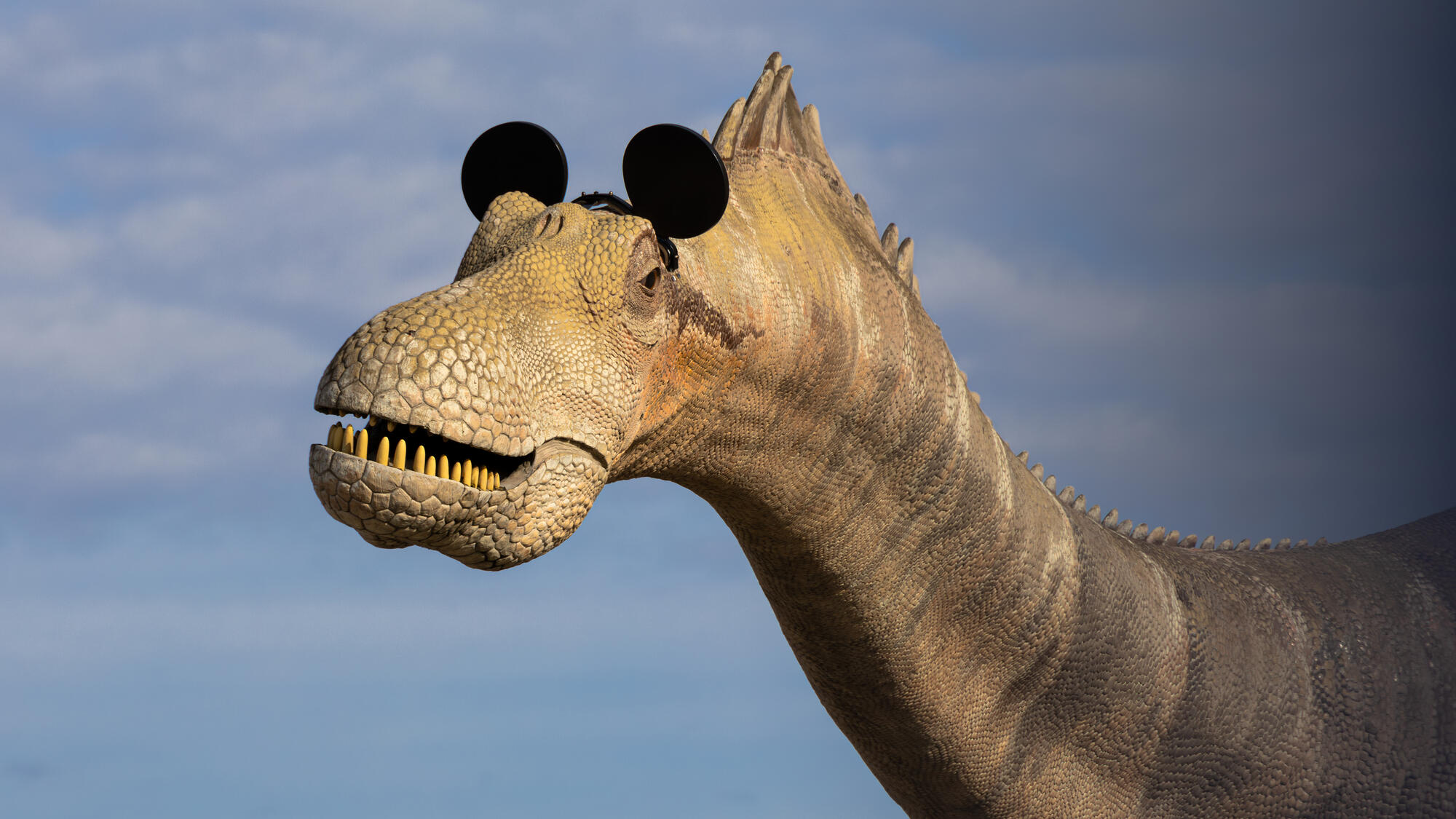 Dinosaur sculpture wearing Mickey Mouse ears.