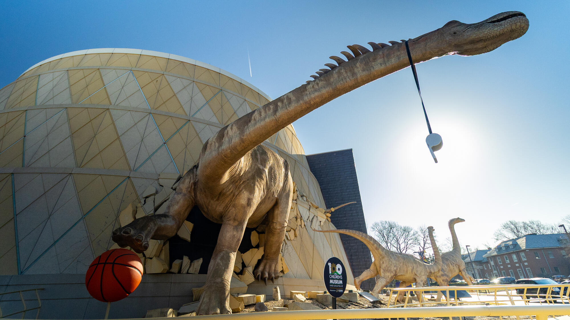 Dinosaur sculpture dribbling an orange basketball.