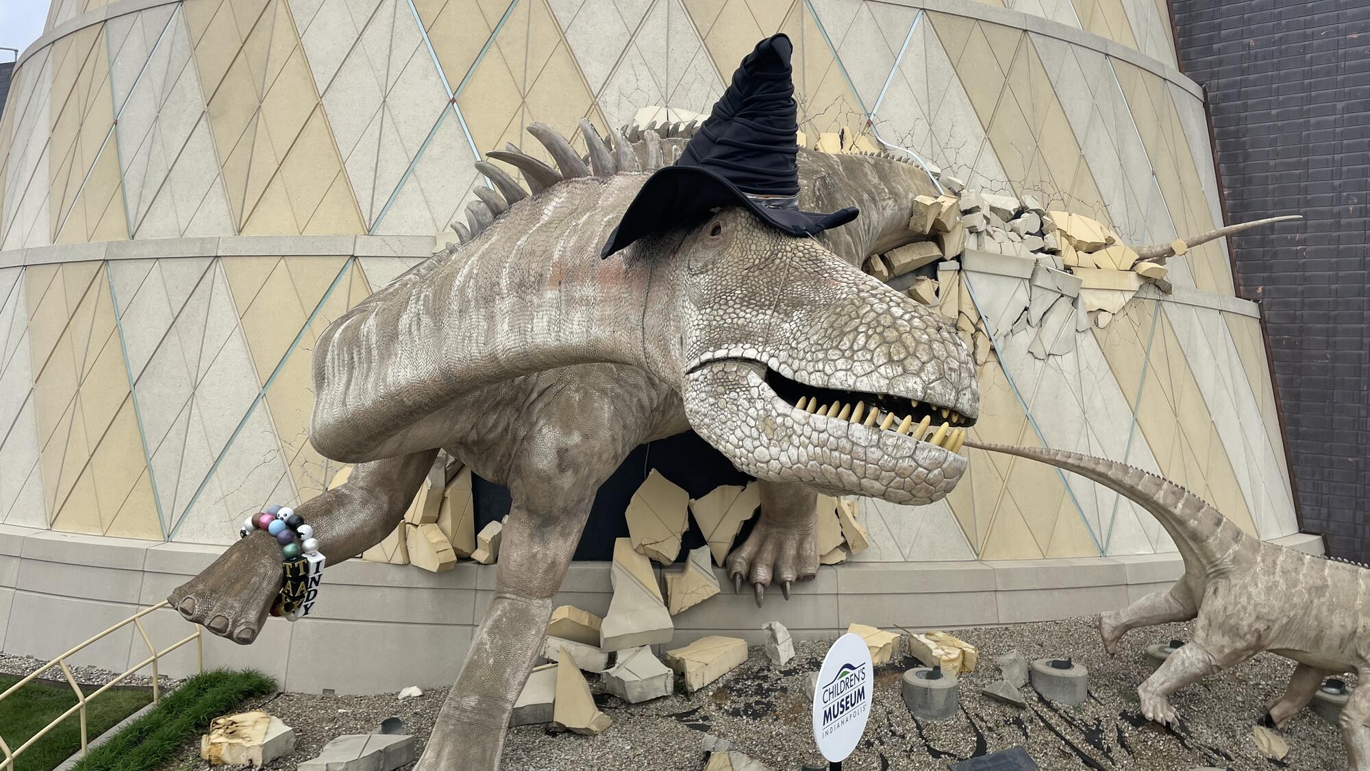 Dinosaur sculpture wearing a black witch hat.