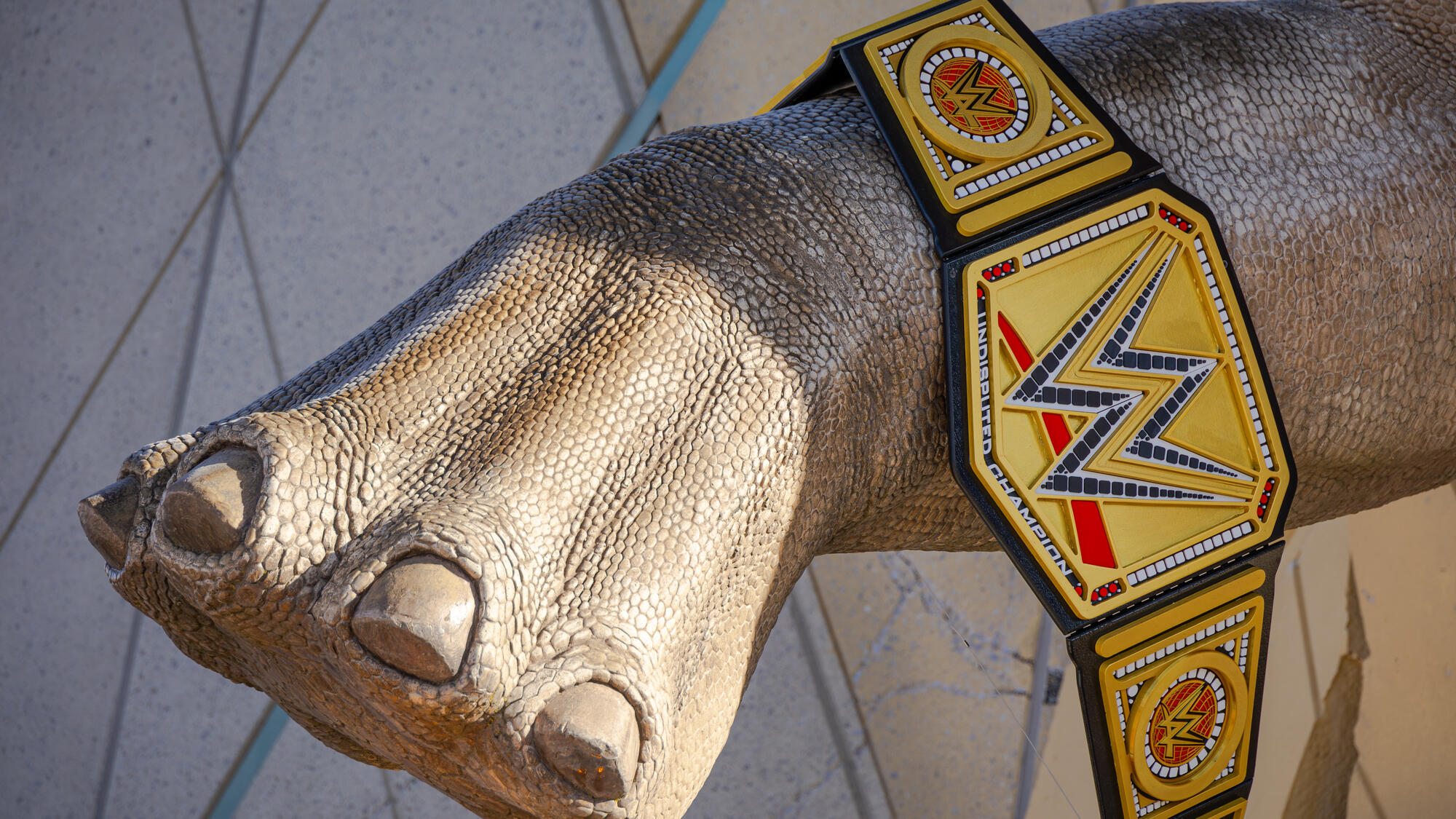 Dinosaur sculpture holding WWE championship belt.