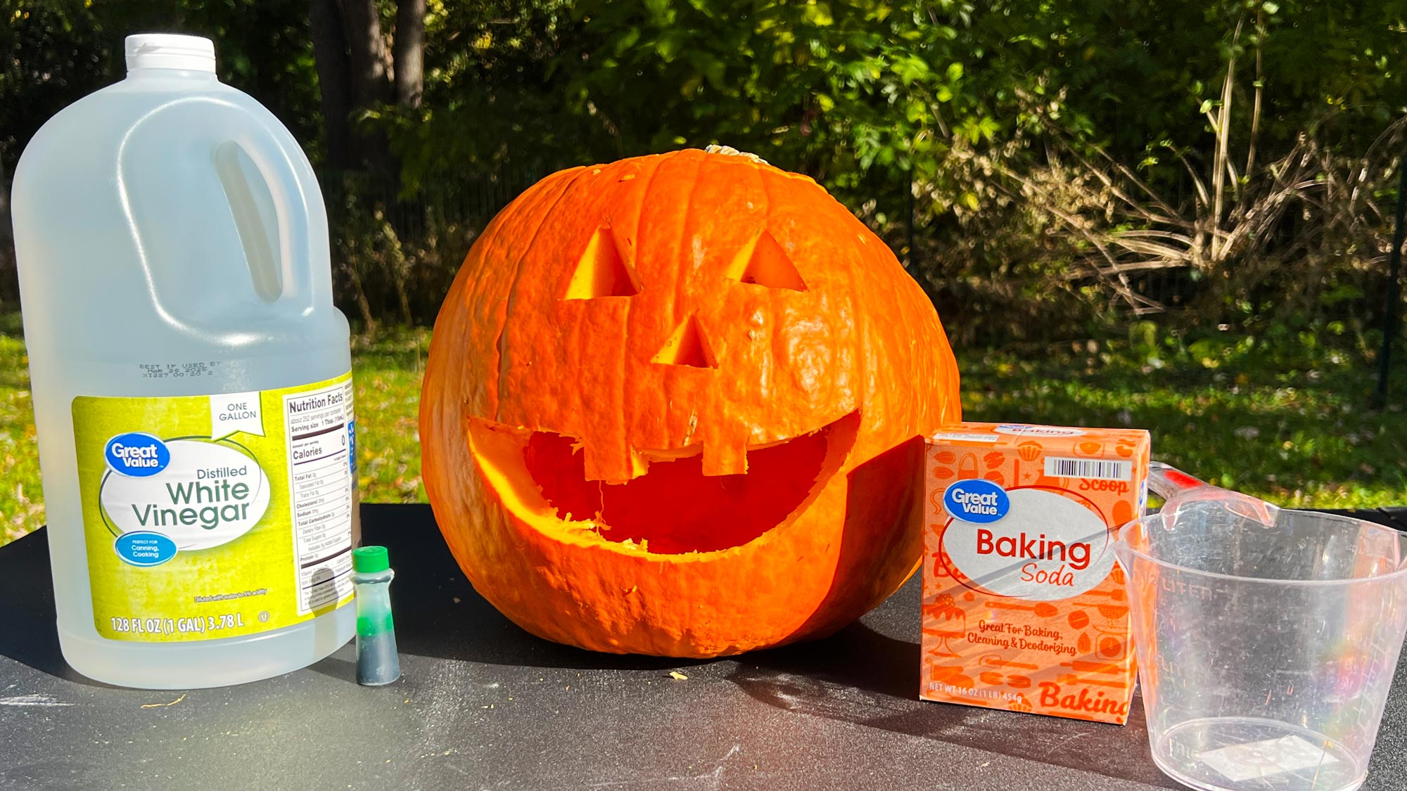 Erupting pumpkin materials: vinegar, food coloring, carved pumpkin, baking soda, and a measuring cup.