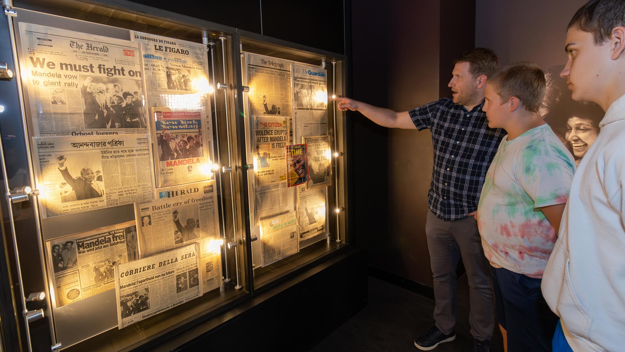 Family looking at wall of newspapers announcing Nelson Mandela's release from prison. 