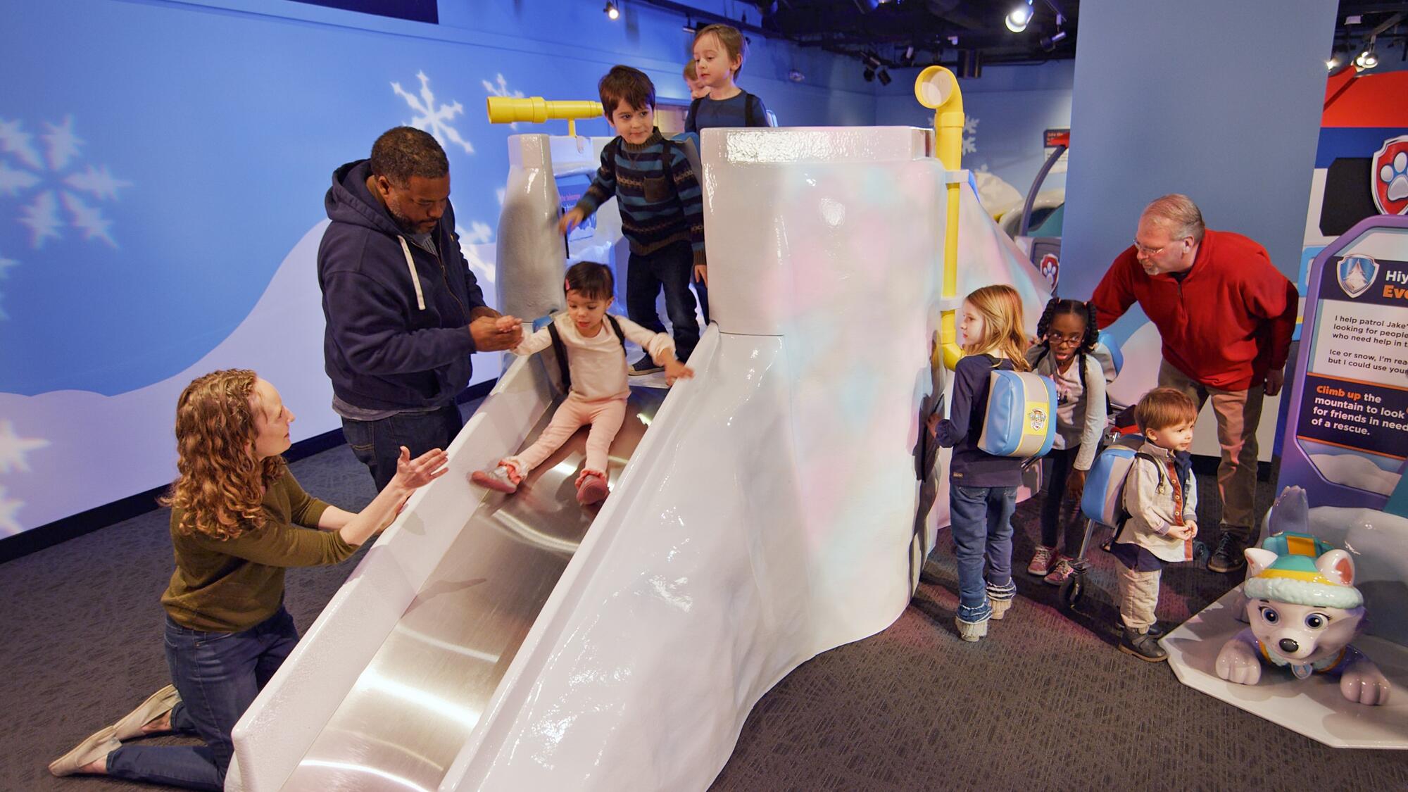 Children playing on and sliding down the Mountain Climber Challenge in the PAW Patrol exhibit.