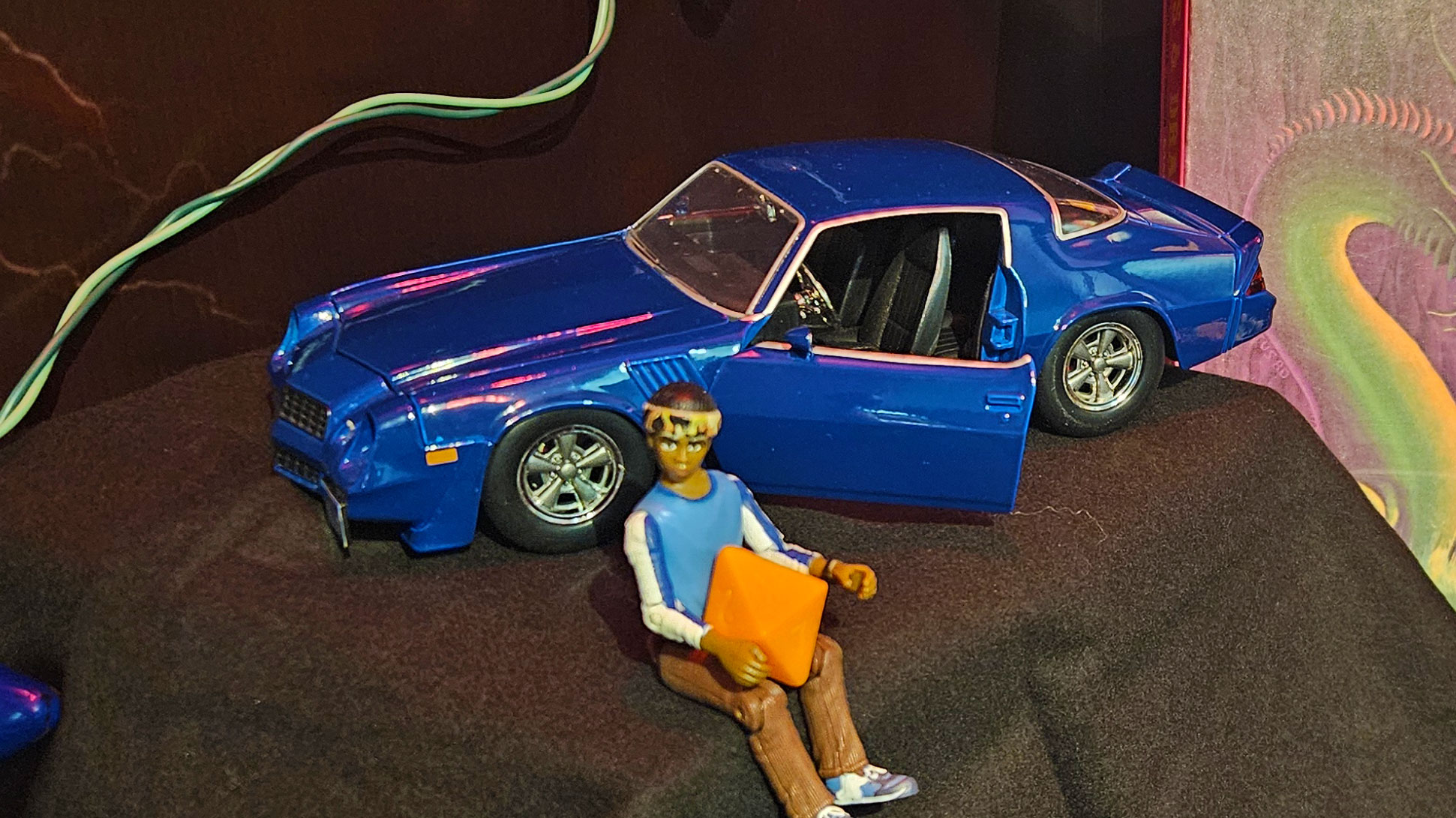 Blue toy Camaro with action figure sitting in front of it.
