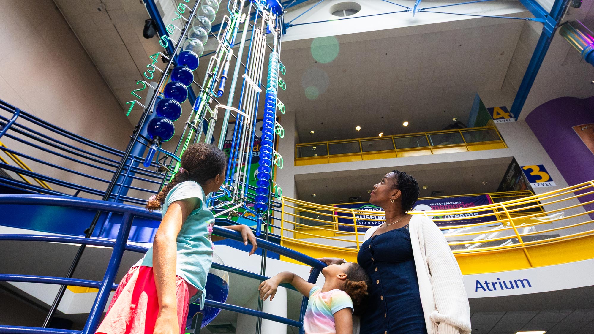 Grown-up and two children looking up at the Water Clock in the Sunburst Atrium at The Children's Museum of Indianapolis.