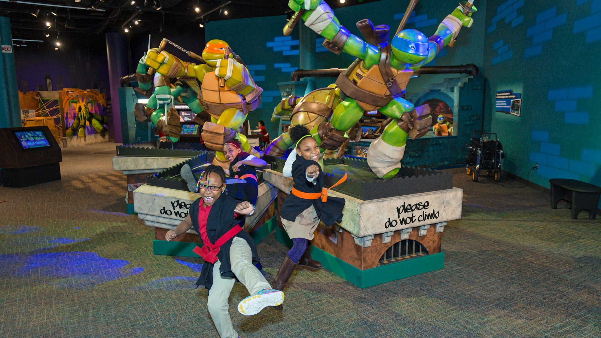 Children posing in front of life-sized sculpts of the Teenage Mutant Ninja Turtles.