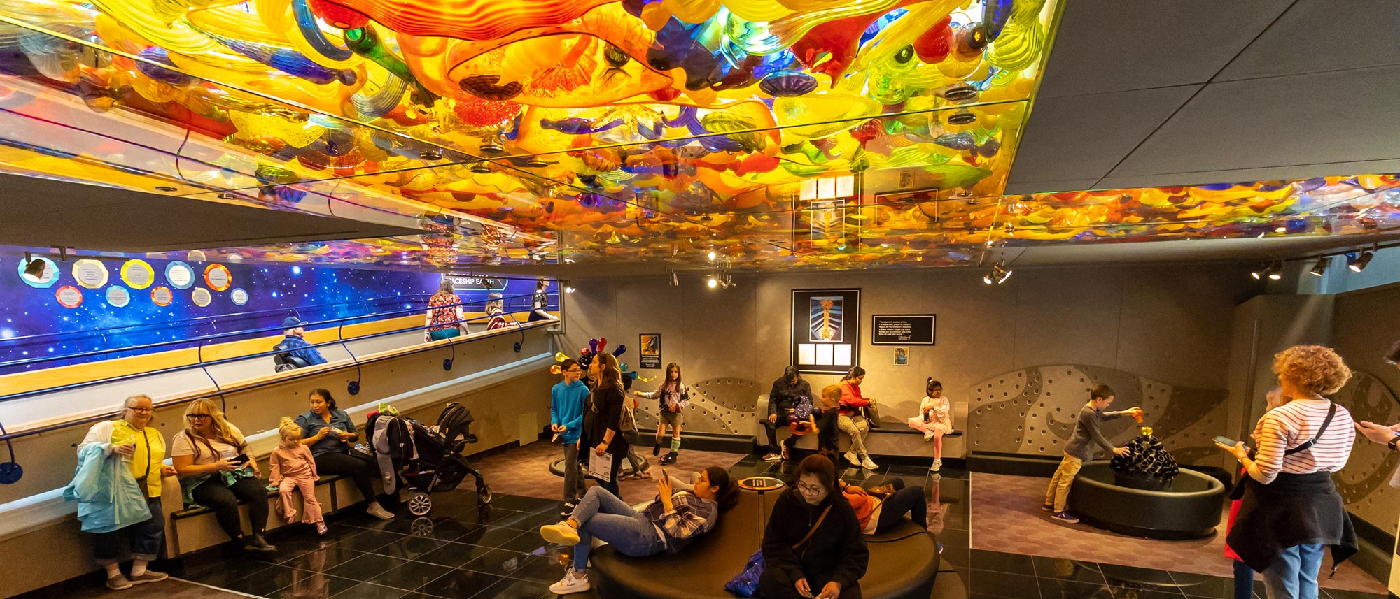 People standing underneath colorful glass ceiling. 