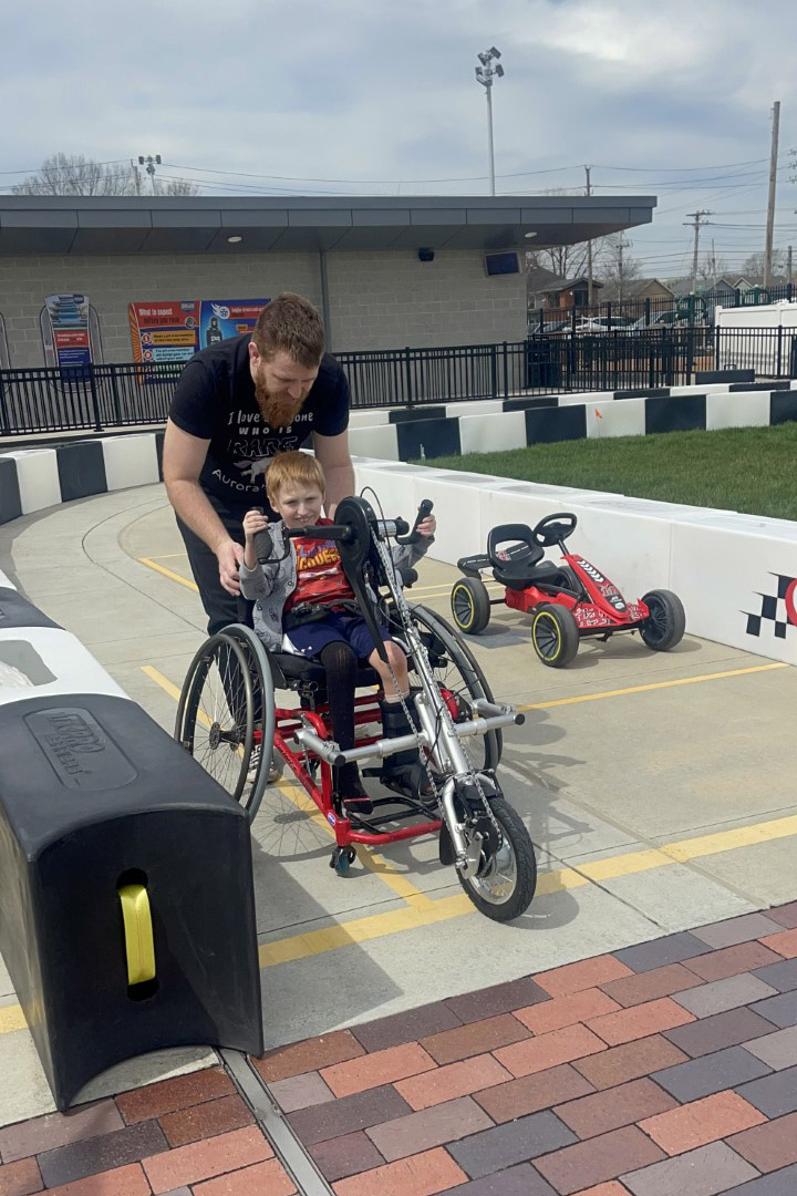 Child using hand pedal attachments to race in wheelchair.