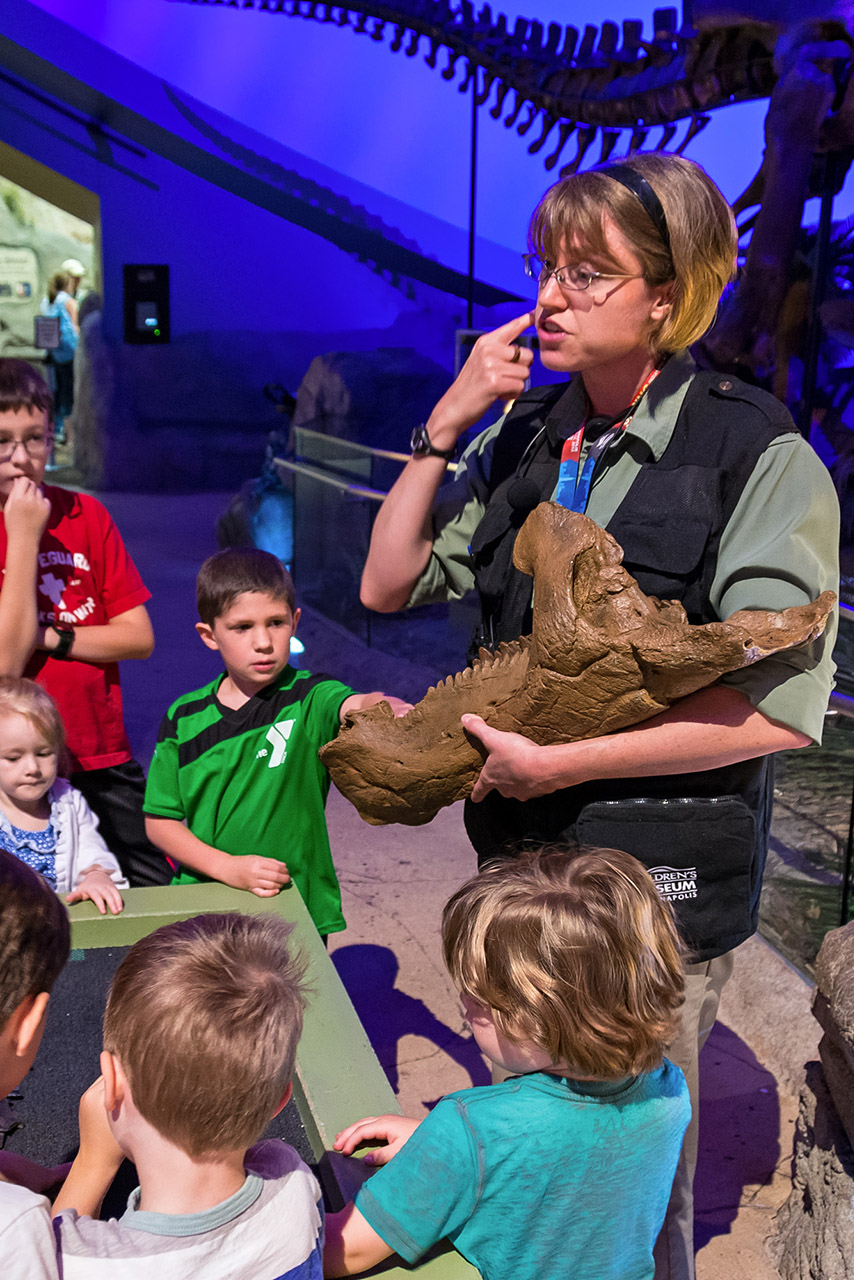 Staff member showing group of children dinosaur fossil.