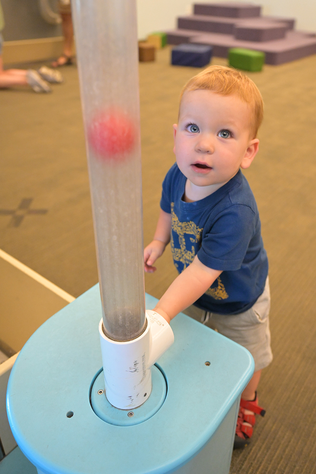 Toddler looking at a clear tube that has a ball inside.