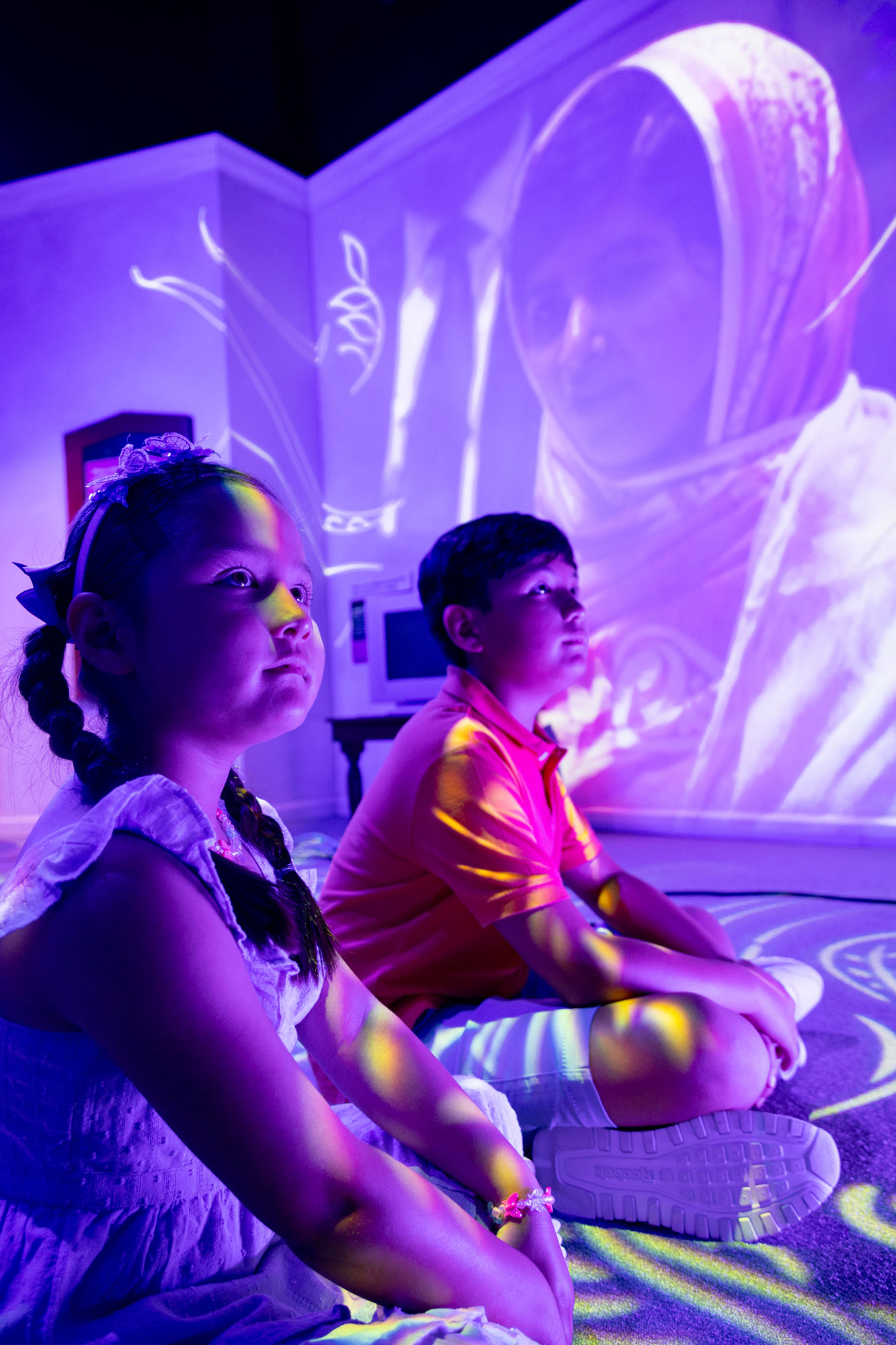 Children sitting down with a projection of Malala Yousufzai on the wall behind them.