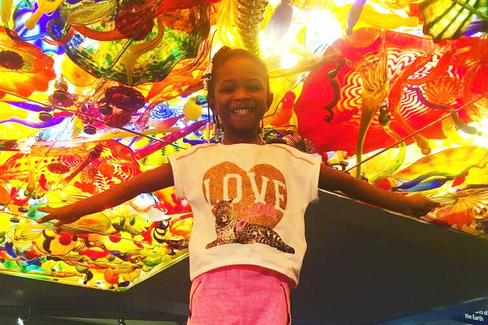 Child with arms stretched wide underneath a colorful glass ceiling.