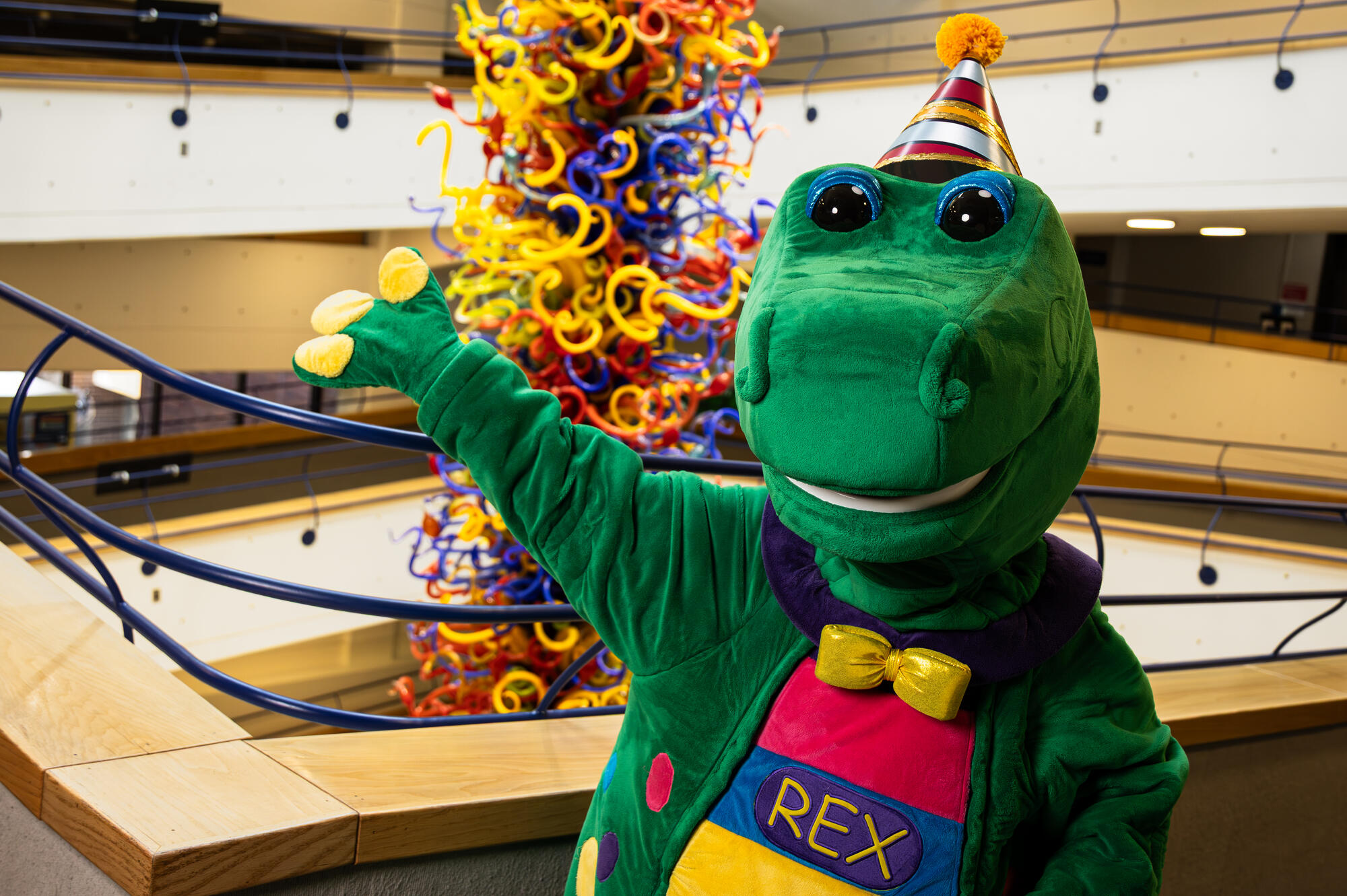 Rex wearing a birthday hat and standing in front of the Chihuly Fireworks of Glass sculpture.