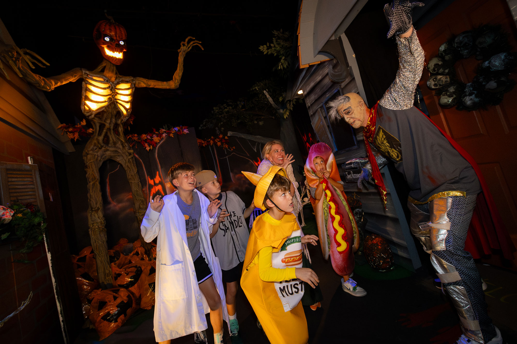 Children screaming at monster with arms raised. Giant glowing skeleton with arms raised is in the background.
