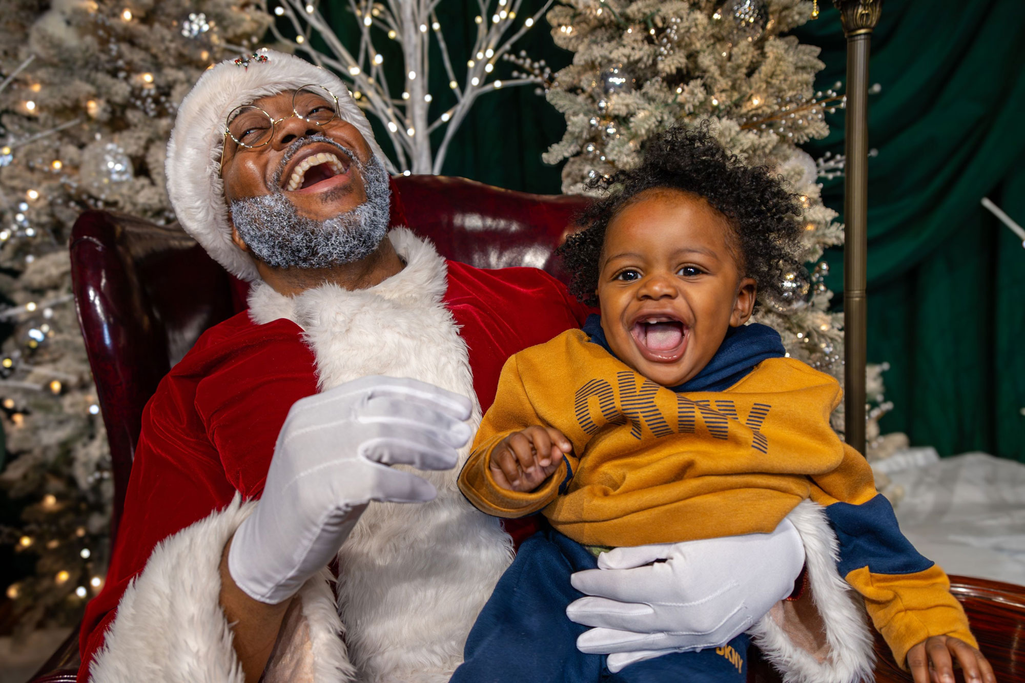 Child sitting on Santa's lap. Child and Santa are laughing.