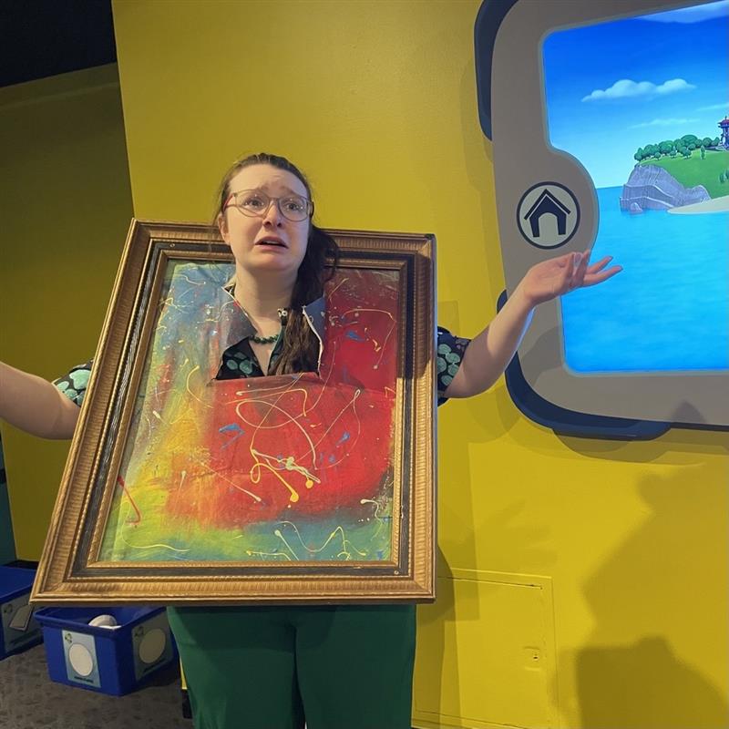 Museum staff member with her head poking through a painting.