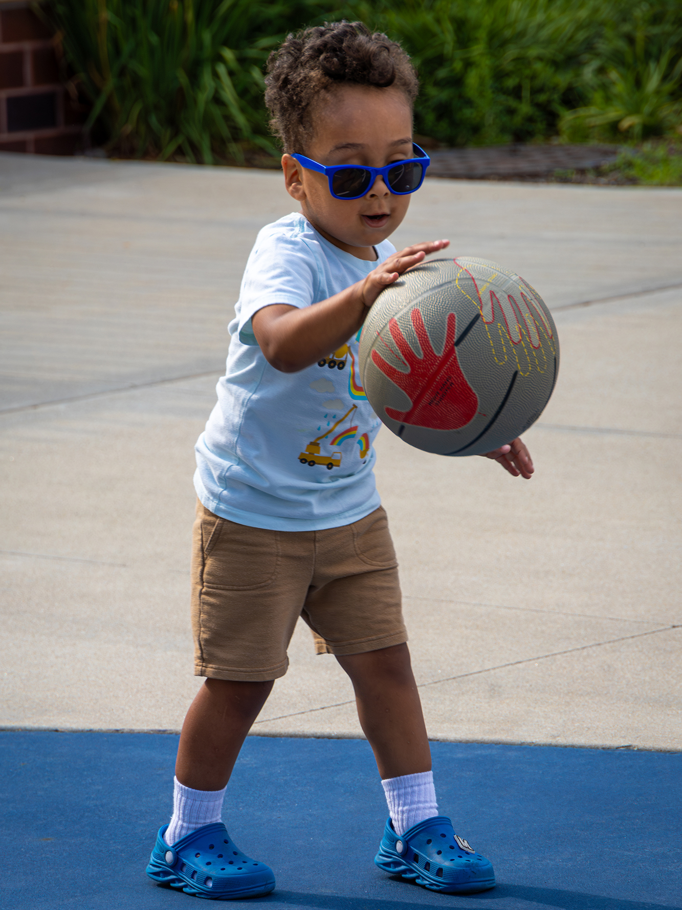 Child wearing sunglasses and dribbling basketball.