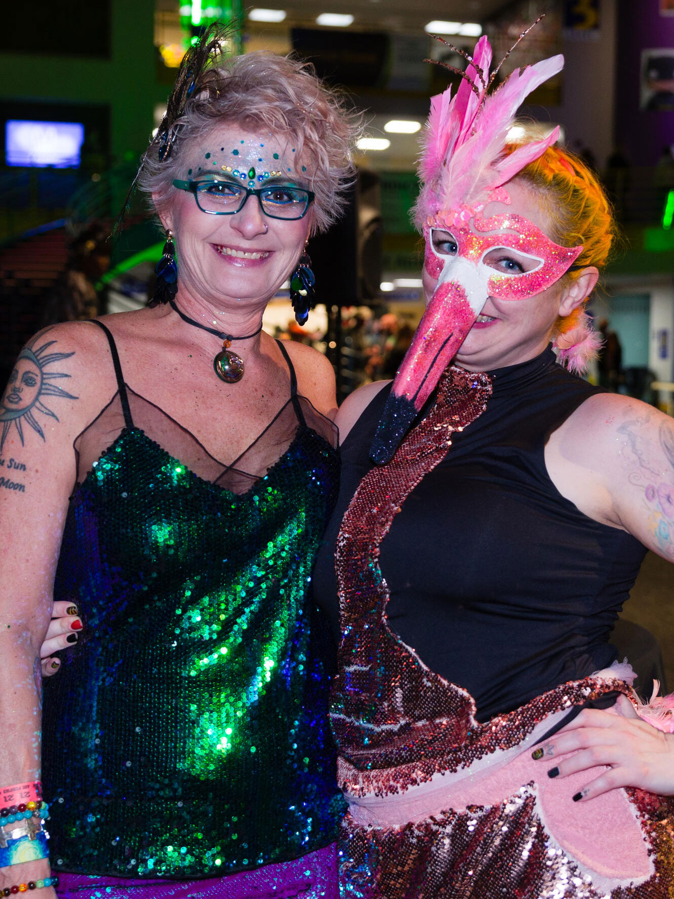 Two smiling women in vibrant costumes pose at an After Dark event.
