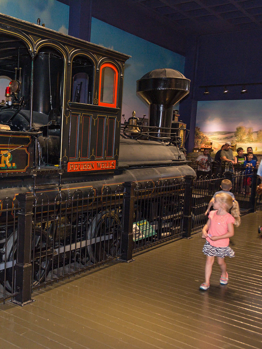 Child standing by Reuben Wells locomotive engine in the All Aboard exhibit.