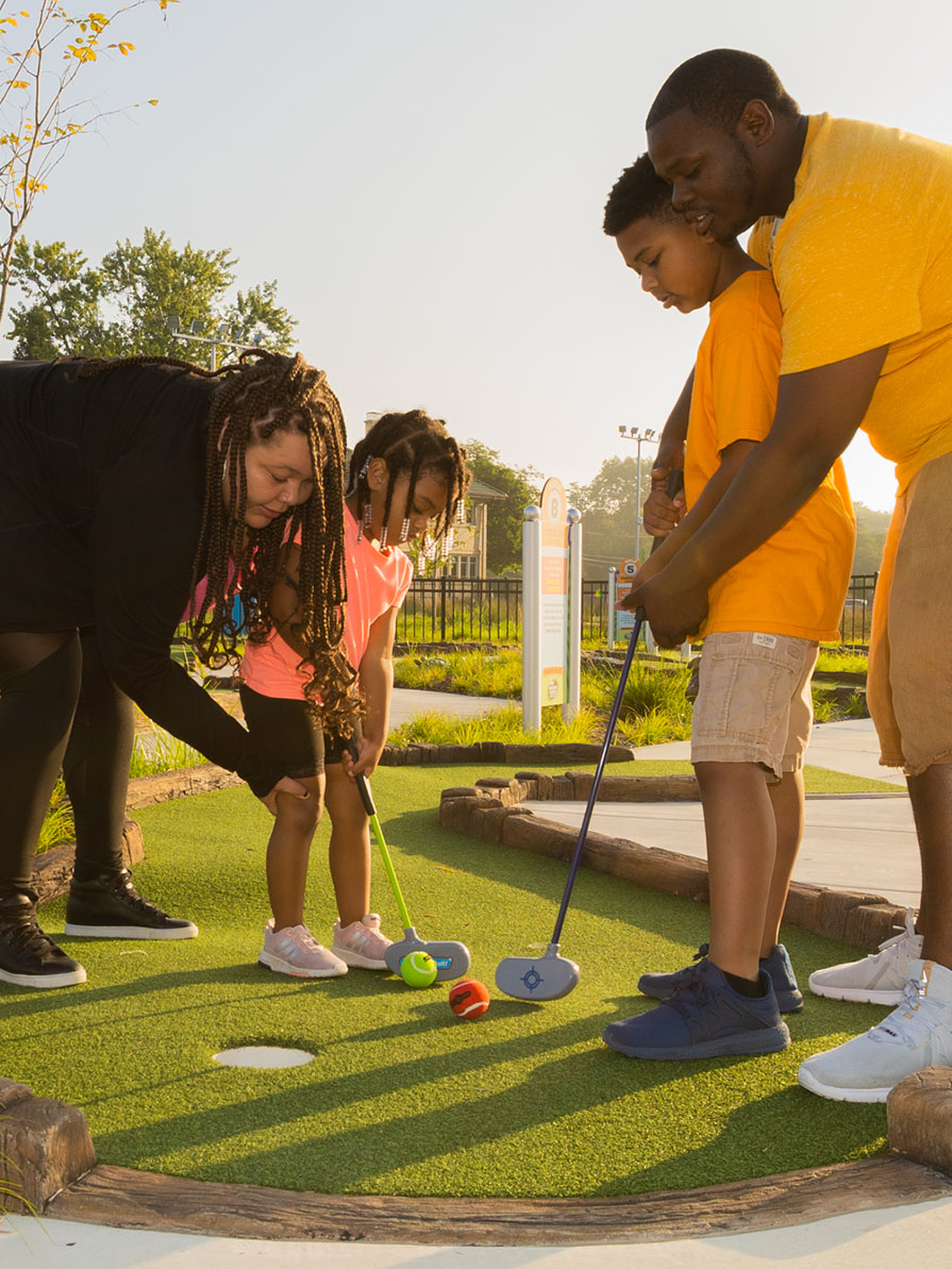 Grown-ups helping children putt golf balls. 