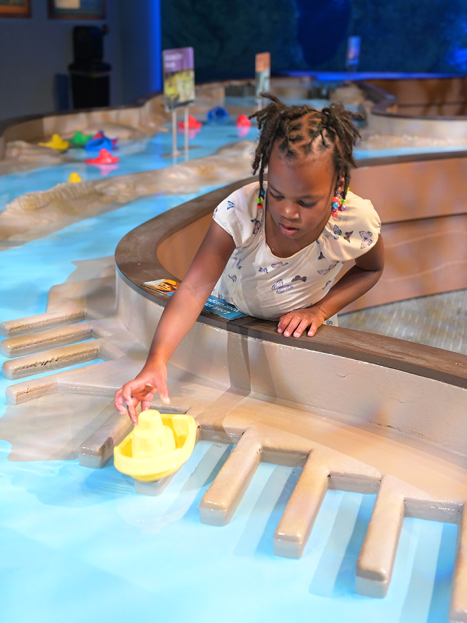 Child reaching for a boat on the water table. 