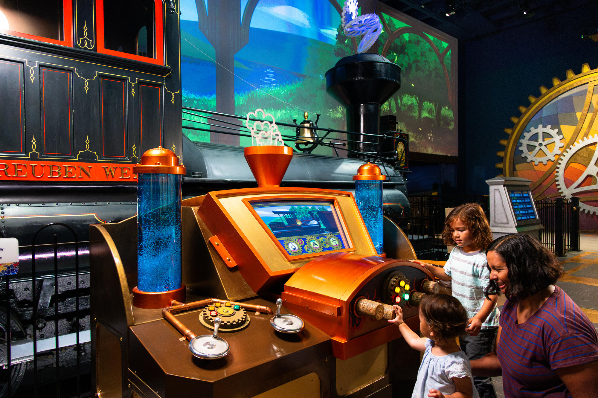 Family playing at a control panel in front of the Reuben Wells steam engine in the All Aboard exhibit.