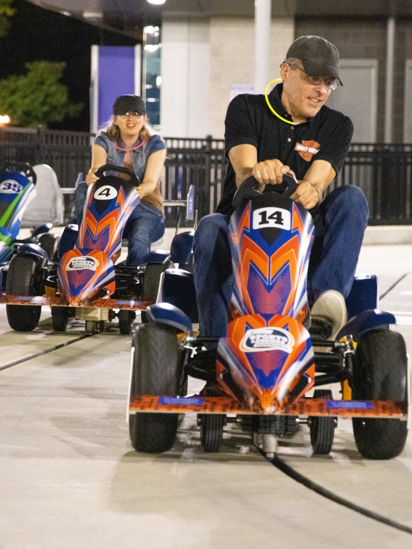 Two adults racing pedal car race cars at an After Dark event.