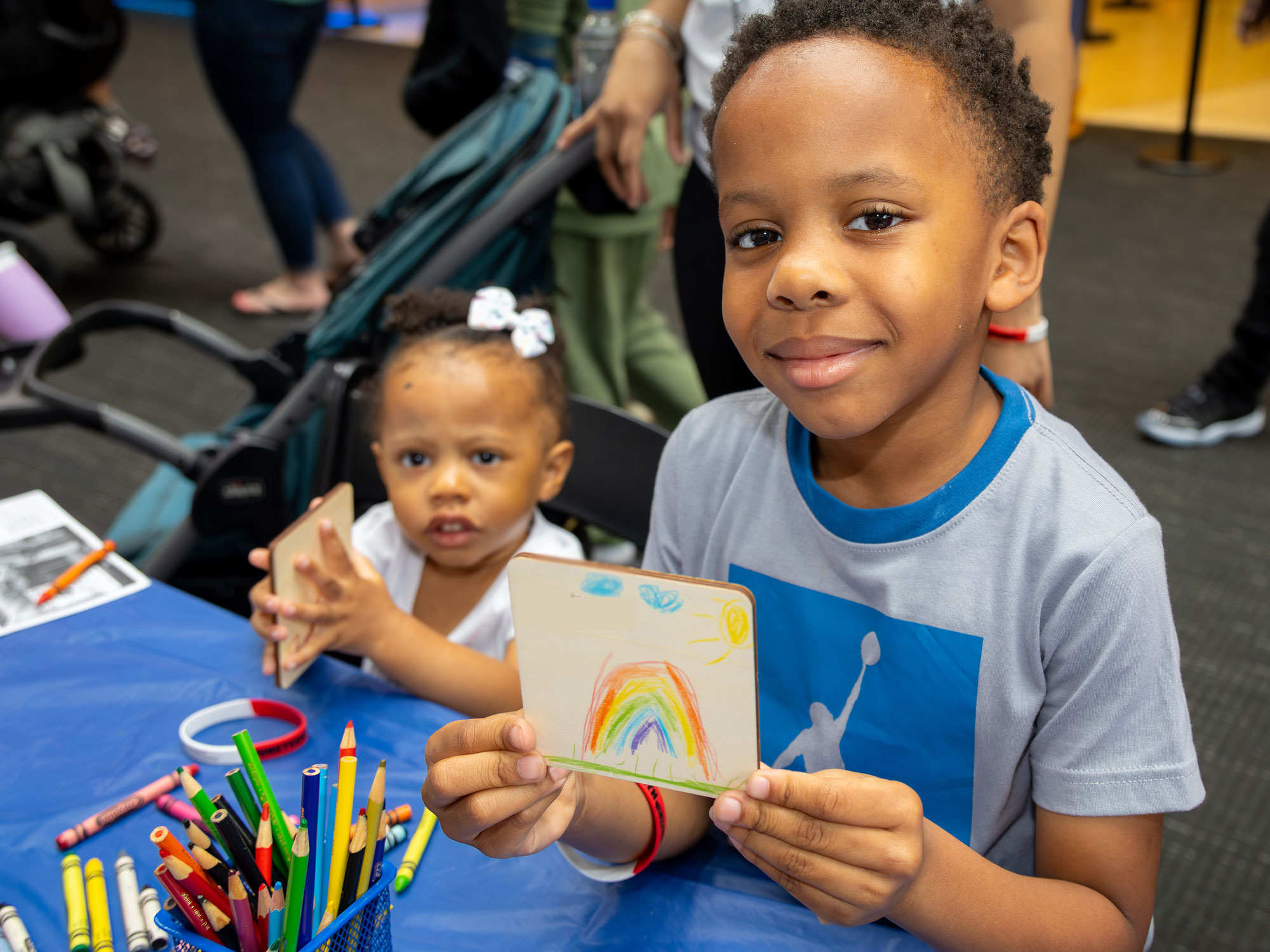 Child holding drawing of rainbow.