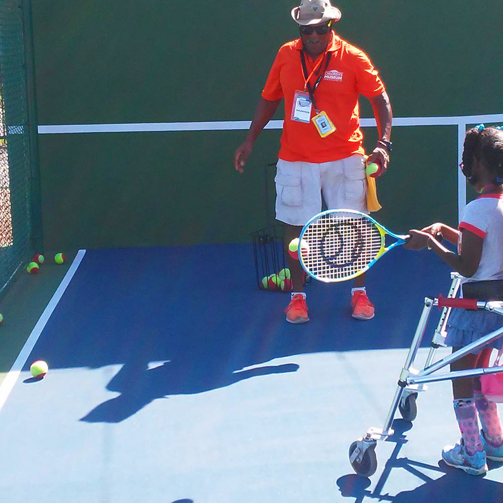 Riley Children's Health Sports Legends Experience coach helping child play tennis at The Children's Museum of Indianapolis