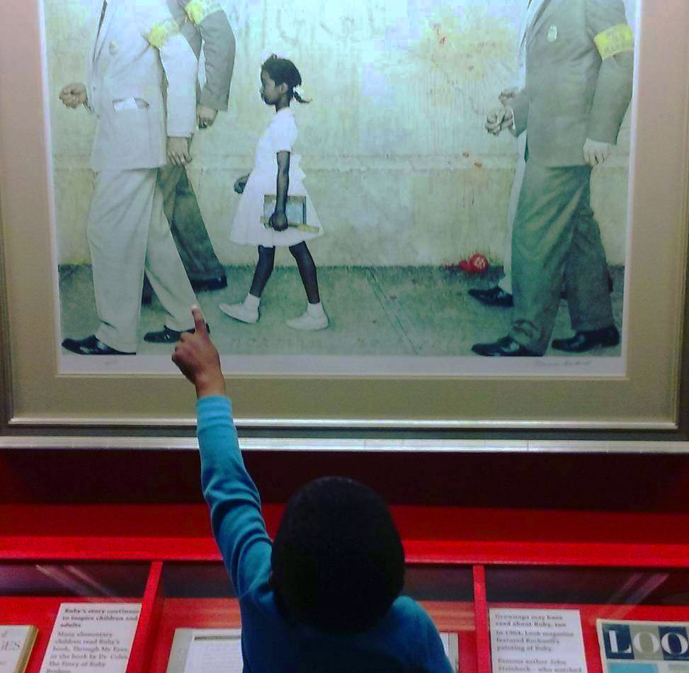 Child pointing at the Norman Rockwell painting The Problem We All Live With in the Ruby Bridges gallery inside The Power of Children exhibit at The Children's Museum of Indianapolis