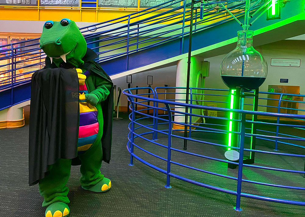 Rex wearing a vampire costume standing by the Water Clock in the Sunburst Atrium at The Children's Museum of Indianapolis