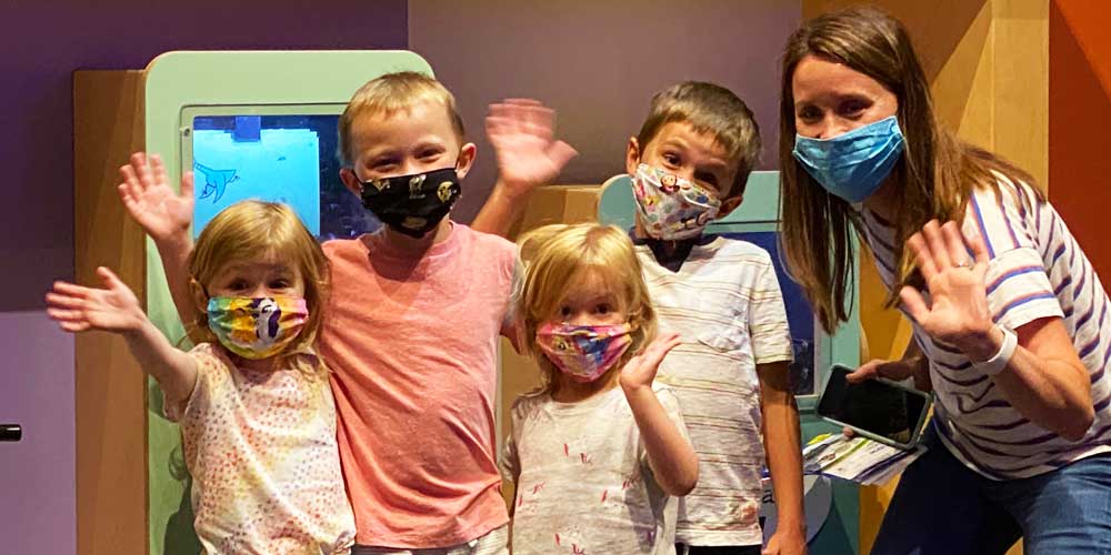 Adult and four children wearing masks and waving.