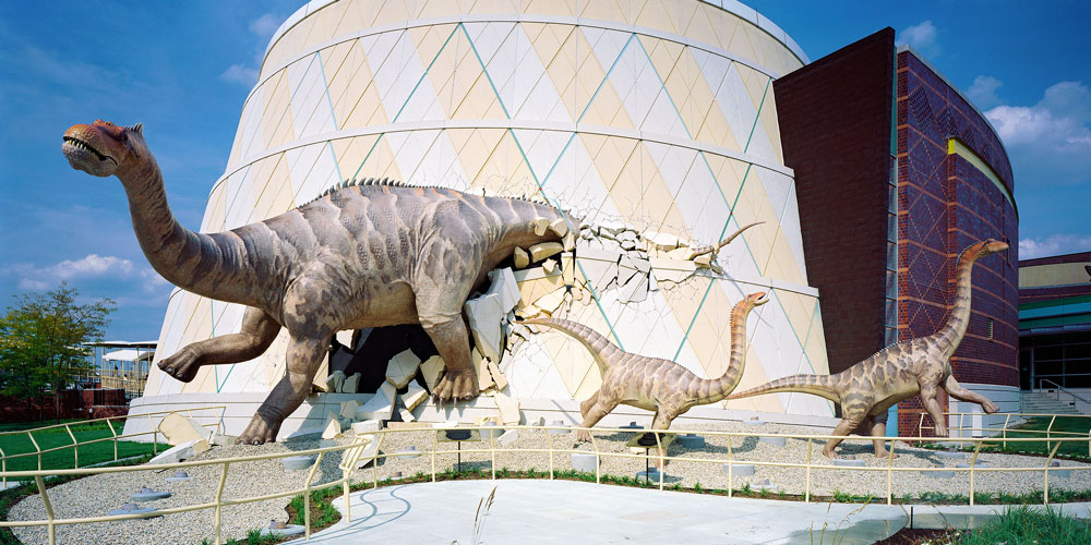 Life-sized sculpture of Alamosaurus family bursting out of the walls of The Children's Museum of Indianapolis