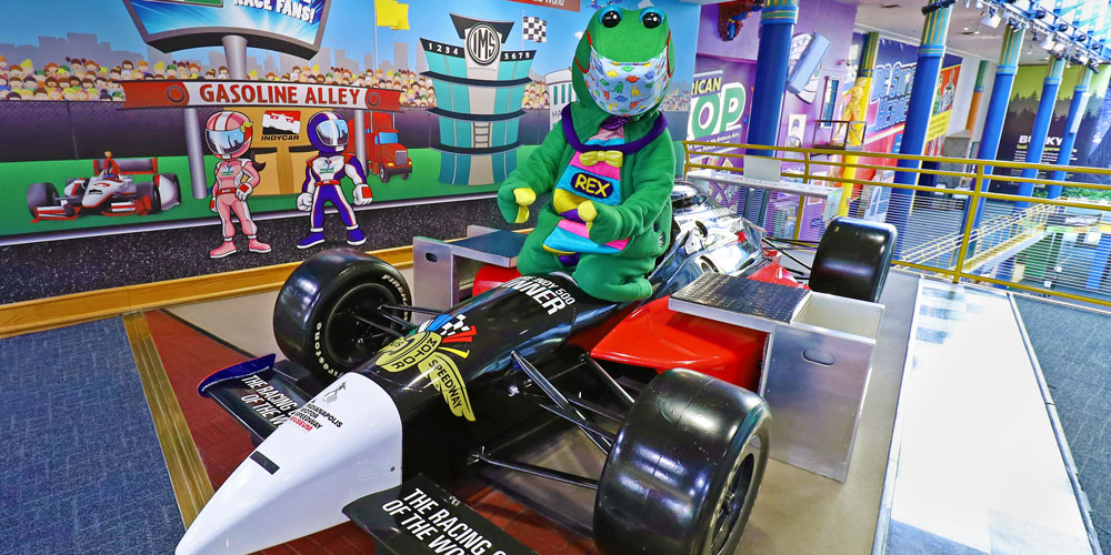 Rex posing near the race car inside The Children's Museum of Indianapolis.