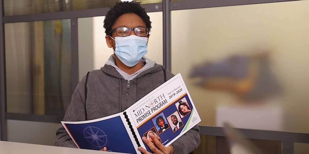 Person wearing glasses and a face mask and looking at an Old National Bank Mid-North Promise Program brochure.