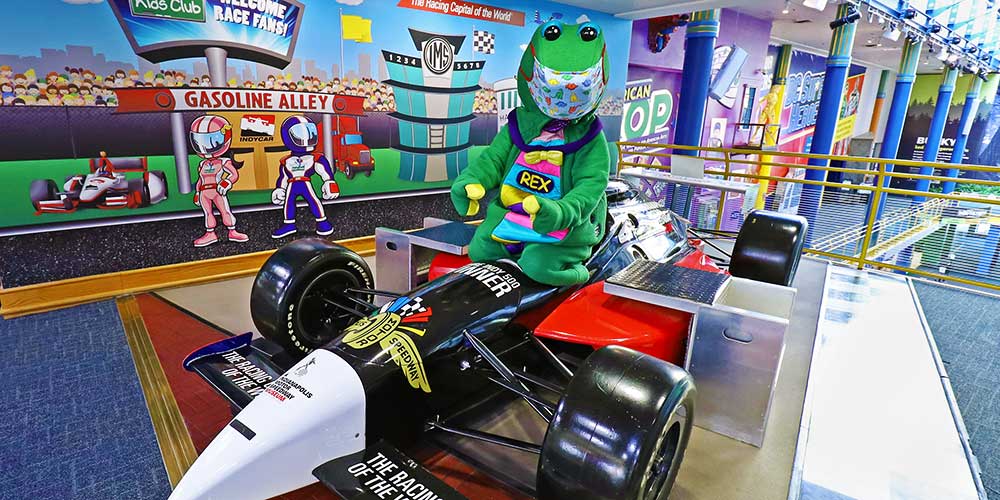 Rex wearing a mask while sitting in the IndyCar show car on display at The Children's Museum of Indianapolis