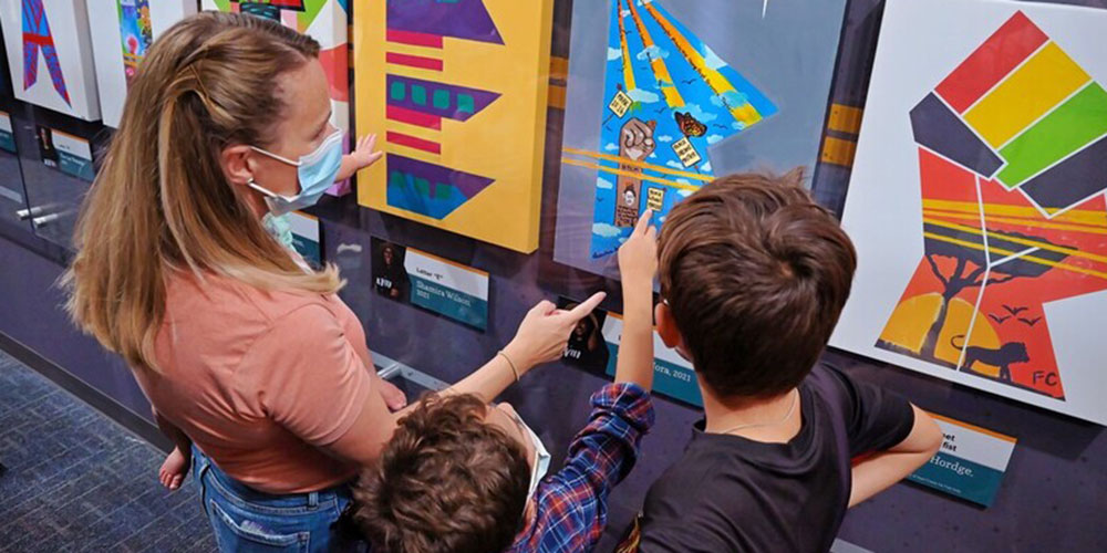 Family examining paintings of letters in the #BLACKLIVESMATTER mural in Stories from Our Community: The Art of Protest