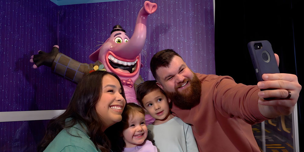 Family posing for a selfie in front of a life sized sculpture of Bing Bong from Pixar's Inside Out.