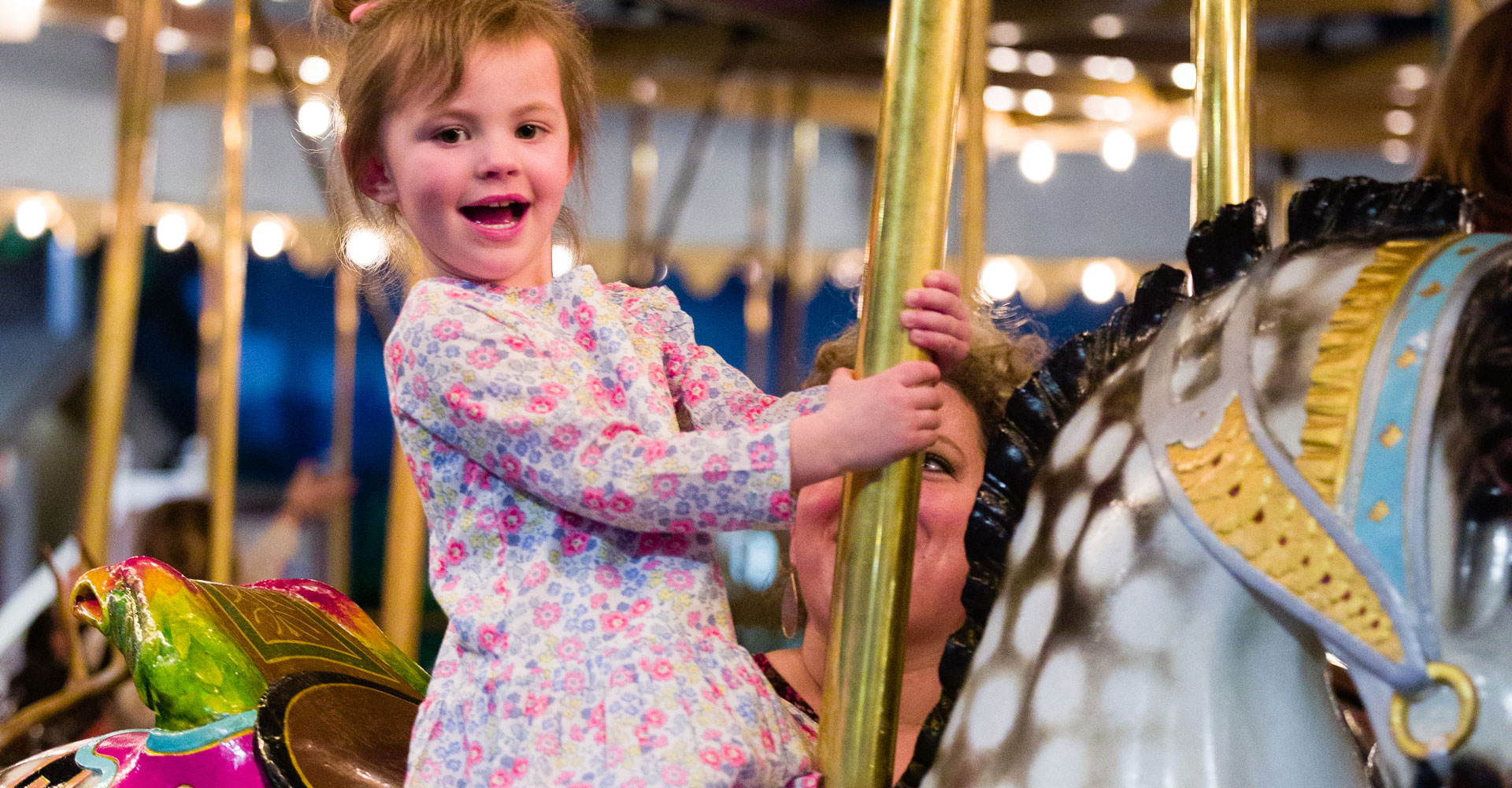 Small child with short brown hair smiling and sitting on a Carousel horse.