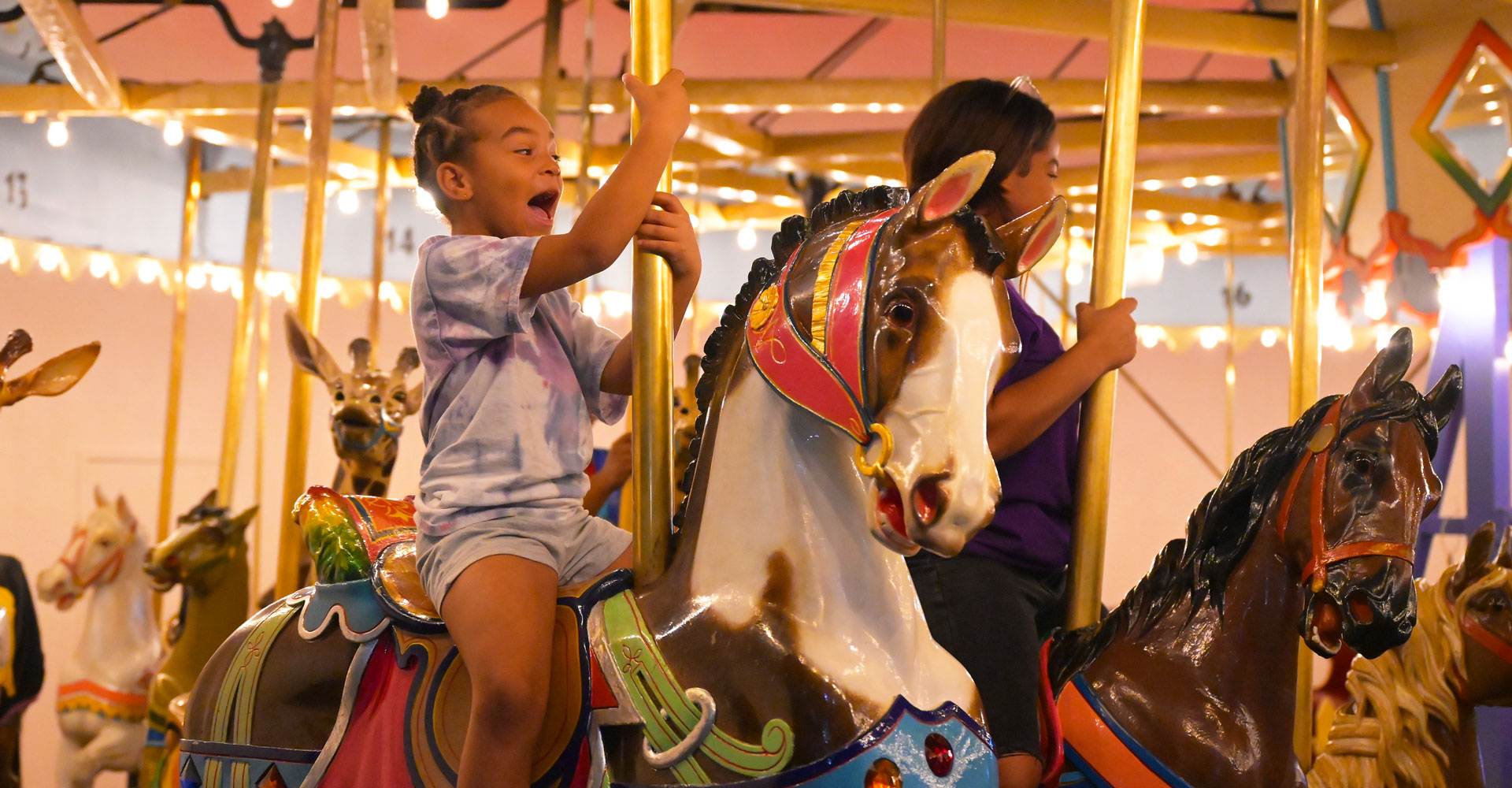 Child riding carousel horse and laughing.