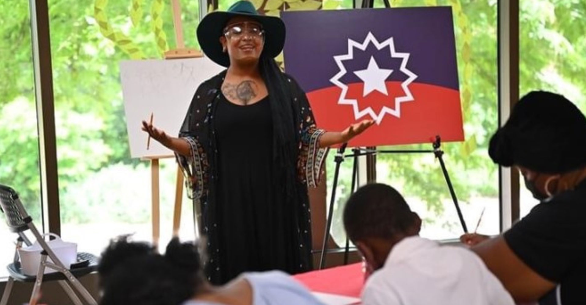 Visiting Artist Deonna Craig standing in front of a class with a Juneteenth flag behind her.