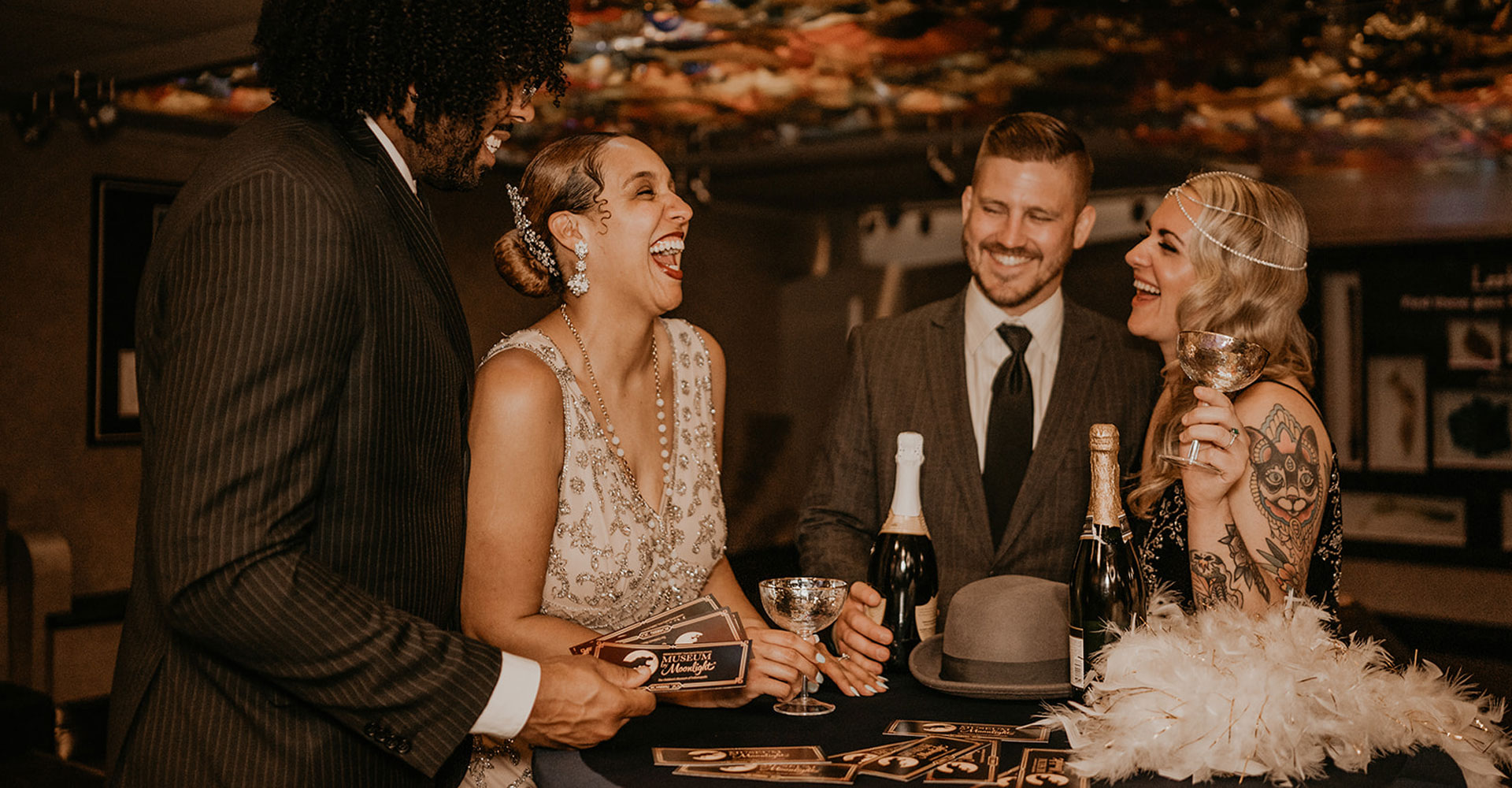 Two couples wearing 1920s inspired clothes are laughing and holding cocktail glasses 