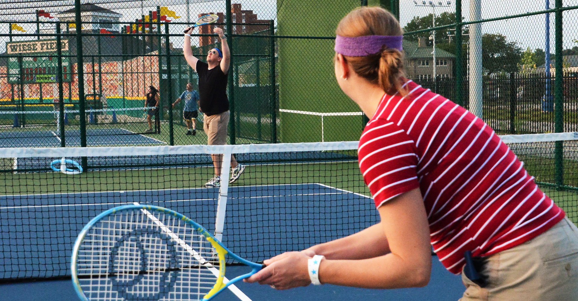 Grown-up playing tennis. One is holding a tennis racquet. Another is holding arms up in victory.
