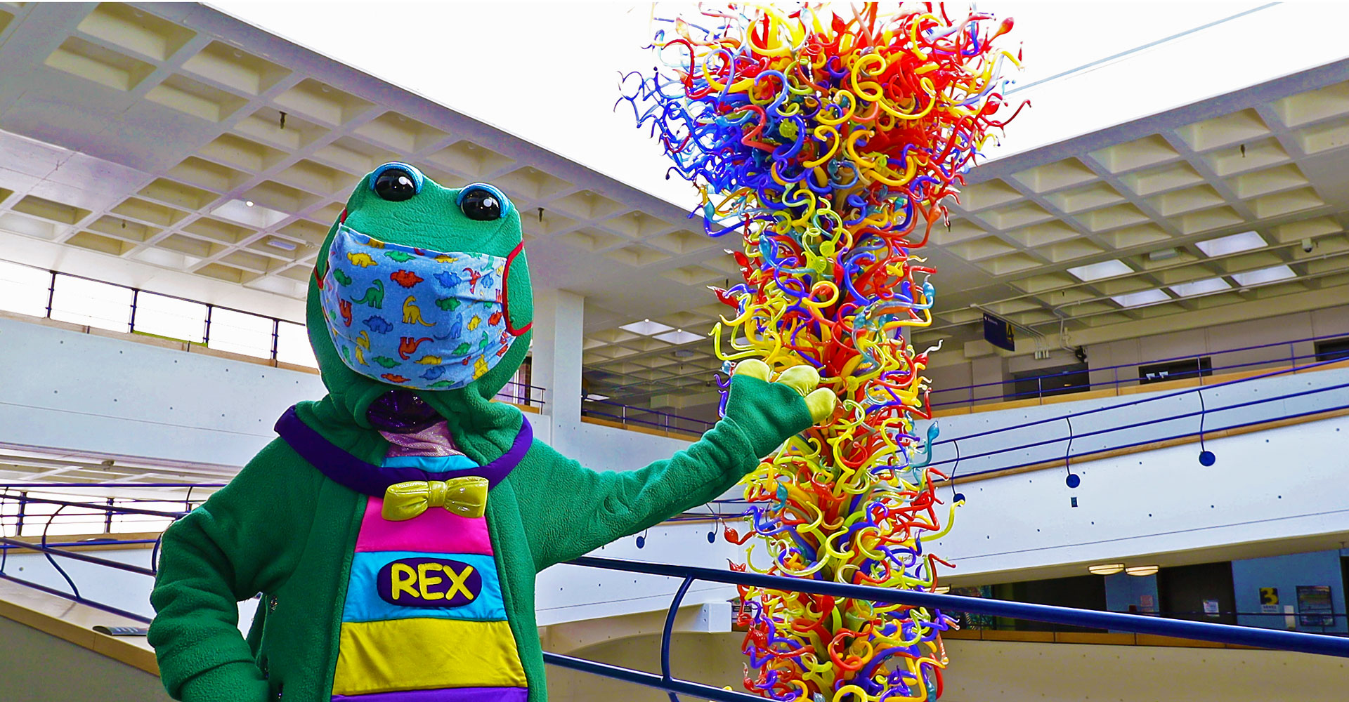 Rex wearing a mask and standing in front of the Chihuly Fireworks of Glass sculpture.