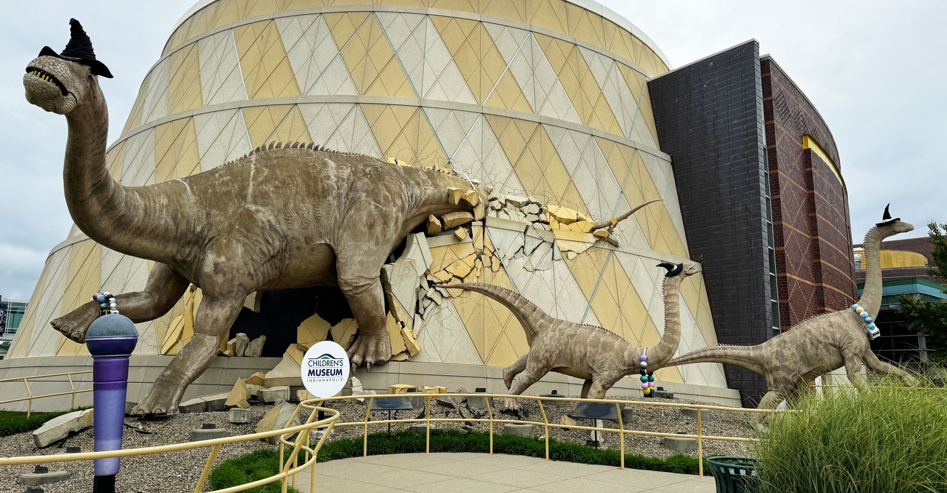 Sculpture of dinosaurs bursting out of the museum with a giant purple microphone and wearing Taylor Swift-inspired friendship bracelets and witches hats.