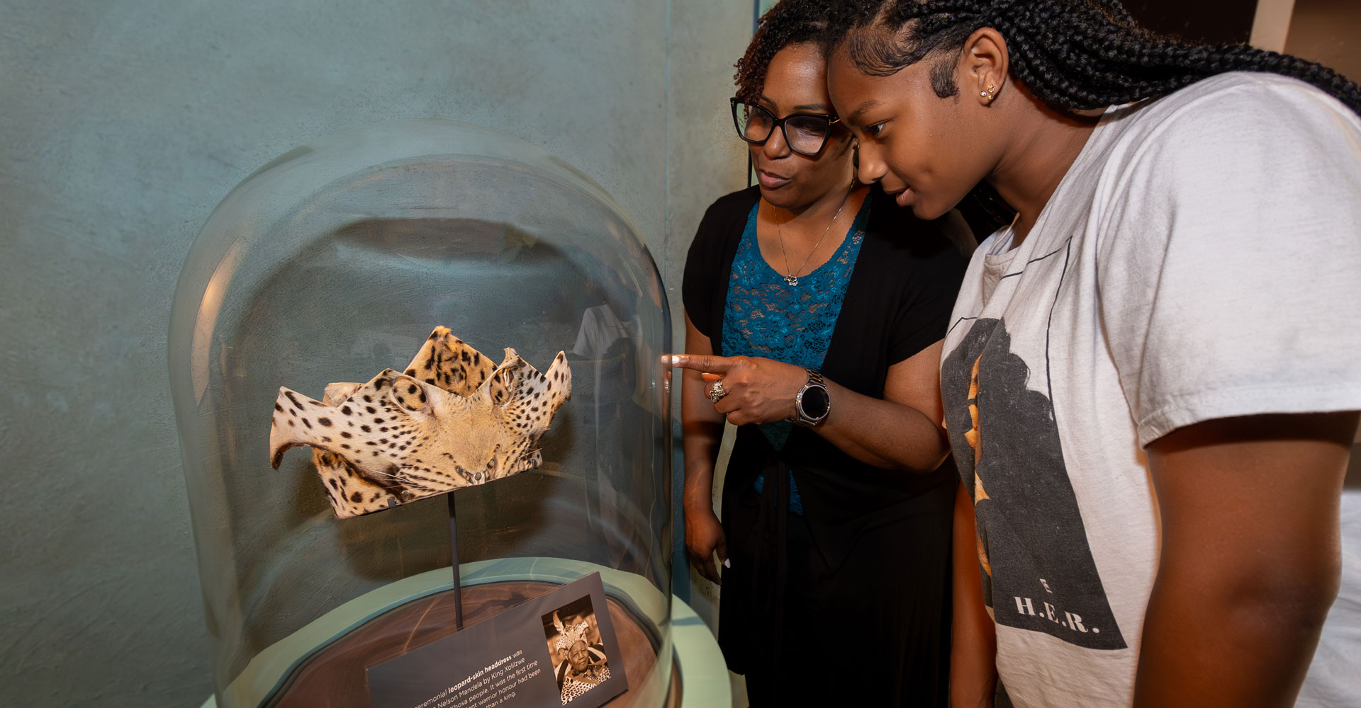 Grown-up and teen looking at Nelson Mandela's ceremonial leopard-skin headdress.