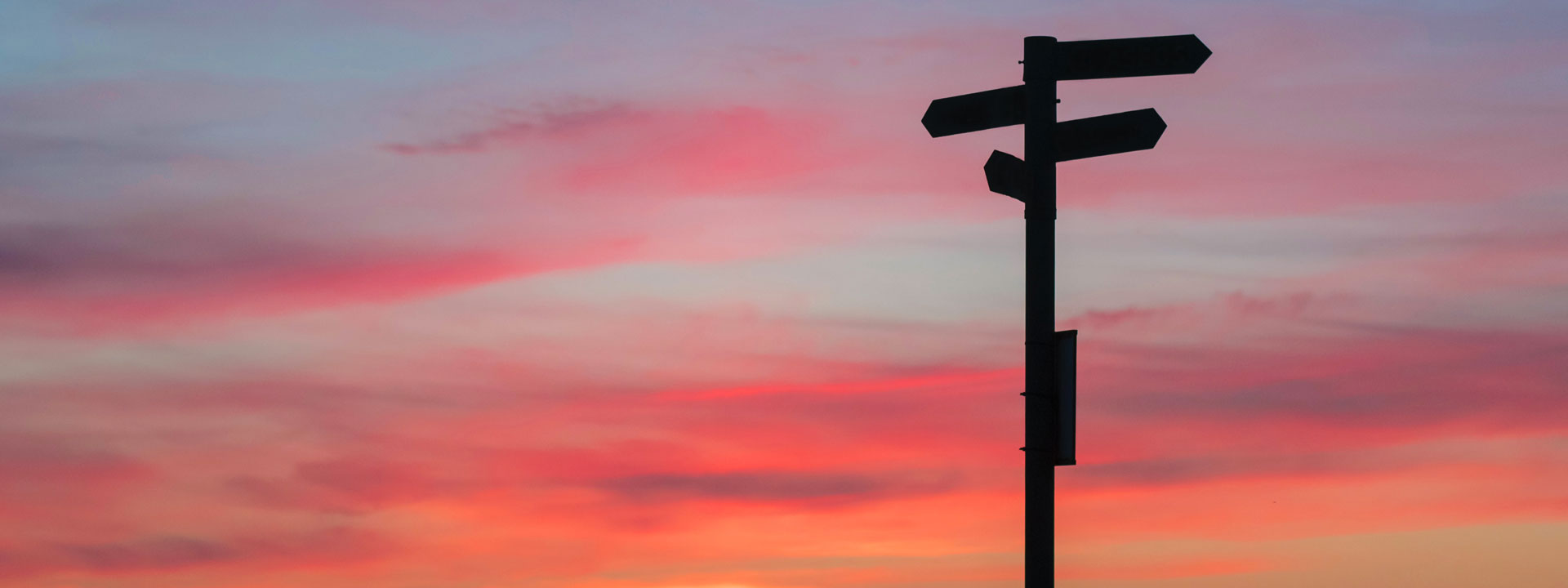 Silhouette of a directional sign against a blue and pink sunrise.