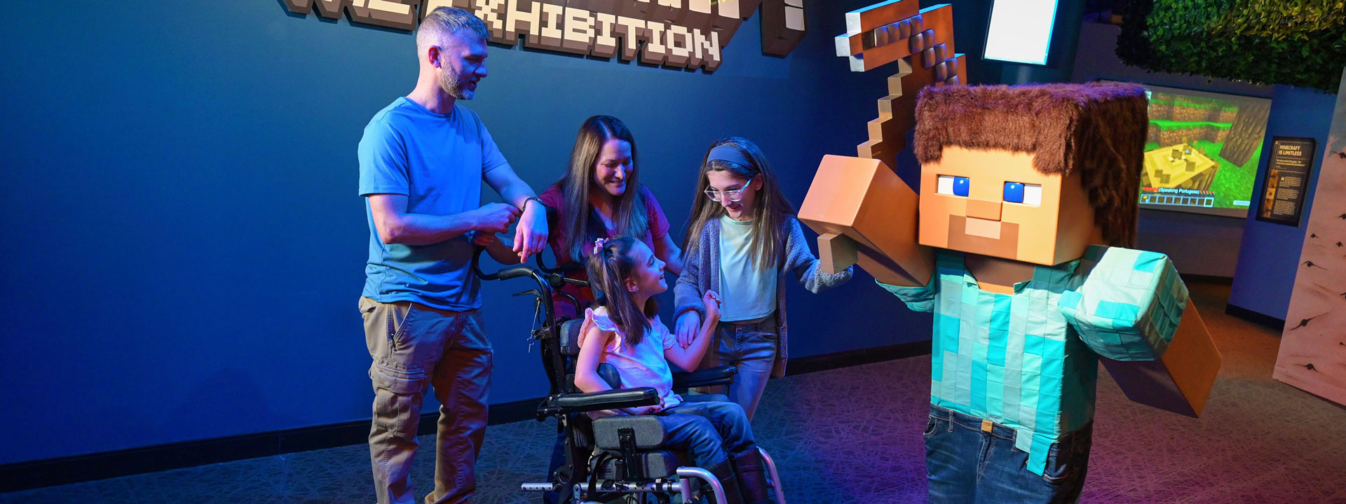 A family is gathered around the entrance to the Minecraft exhibit admiring the Steve statue. 